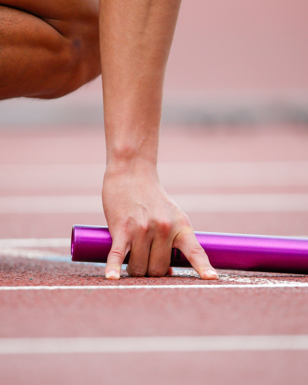 Läufer kniet in Startposition auf der Tartanbahn und hält einen Staffelstab in der Hand., © stock.adobe.com -  D maborosi