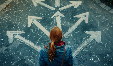 Eine Frau steht an einem Weg, auf dem mehrere Pfeile in unterschiedliche Richtungen zeigend, abgebildet sind, &copy; Adobe Stcok