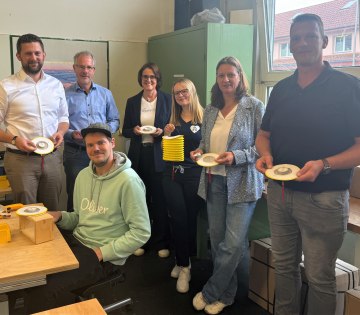 Neues Sozialprojekt der Stadt Bad Salzuflen mit der „Lebenshilfe Detmold e.V. Werre Werkstatt“ für die „Nacht
der 10.000 Kerzen“ am 29. August 2025: Werre Werkstatt-Mitarbeiter Eduard Peters (sitzend) verklebt an seinem Arbeitsplatz
Teelichter mit Zuglaternen. Die fertigen Laternen präsentieren voller Freude (stehend von links) Maximilian Seidel
(Kaufmännischer Vorstand Detmolder Lebenshilfe e.V. Werre Werkstatt), Udo Schwens (Werkstattleiter Detmolder Lebenshilfe e.V.), Myriam Heidemann (Fachdienstleitung Kulturelle Bildung, Event und Stadtmarketing), Francesca Rackow
(Projektmanagerin Eventabteilung Stadt Bad Salzuflen), Stephanie Kleine (Pädagogische Vorständin Detmolder Lebenshilfe e.V. Werre Werkstatt) und Stefan Gehrmann (Arbeitsvorbereitung & Auftragsverwaltung Detmolder Lebenshilfe e.V.
Werre Werkstatt)., © Stadt Bad Salzuflen