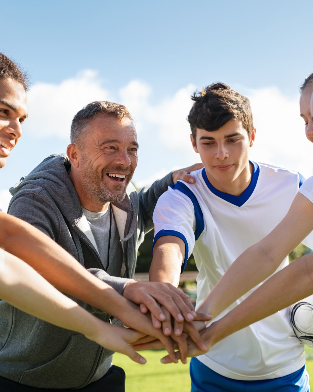 Sportler und Sportlerinnen stehen im Kreis zusammen und legen die Hände aufeinander., © stock.adobe.com - Rido