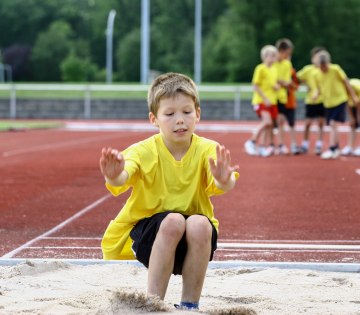 Ein Kind springt beim Weitsprung in eine Sandgrube., © stock.adobe.com - Alexandra