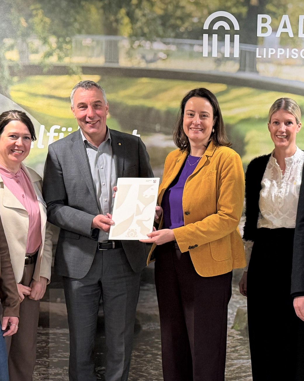 Neuer Meilenstein f&uuml;r die touristische Weiterentwicklung in Bad Salzuflen: Regierungspr&auml;sidentin Anna Katharina B&ouml;lling (3.v.r.) &uuml;bergab den F&ouml;rderbescheid f&uuml;r das Zukunftsprojekt &bdquo;Erlebniswelt Kneipp&ldquo; im Landschaftsgarten an B&uuml;rgermeister Dirk Tolkemitt (3.v.l.), Melanie Koring (2.v.r., Erste Beigeordnete & Stadtk&auml;mmerin), Ulrike Niebuhr (links, Technische Beigeordnete), Ralf Hammacher (rechts, Fachbereichsleitung Tourismus, Gesundheit, Kultur) und Katja M&ouml;nnigmann-Steinbeck (2.v.l., Fachbereichsleitung Jugend, Soziale Dienste, Schule). , &copy; Stadt Bad Salzuflen