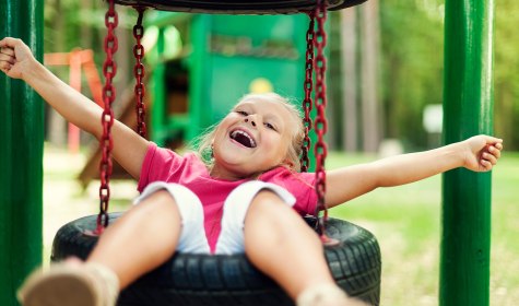 Ein Kind schaukelt mit in die Luft gestreckten Armen auf einer Reifenschaukel., © gpointstudio - stock.adobe.com