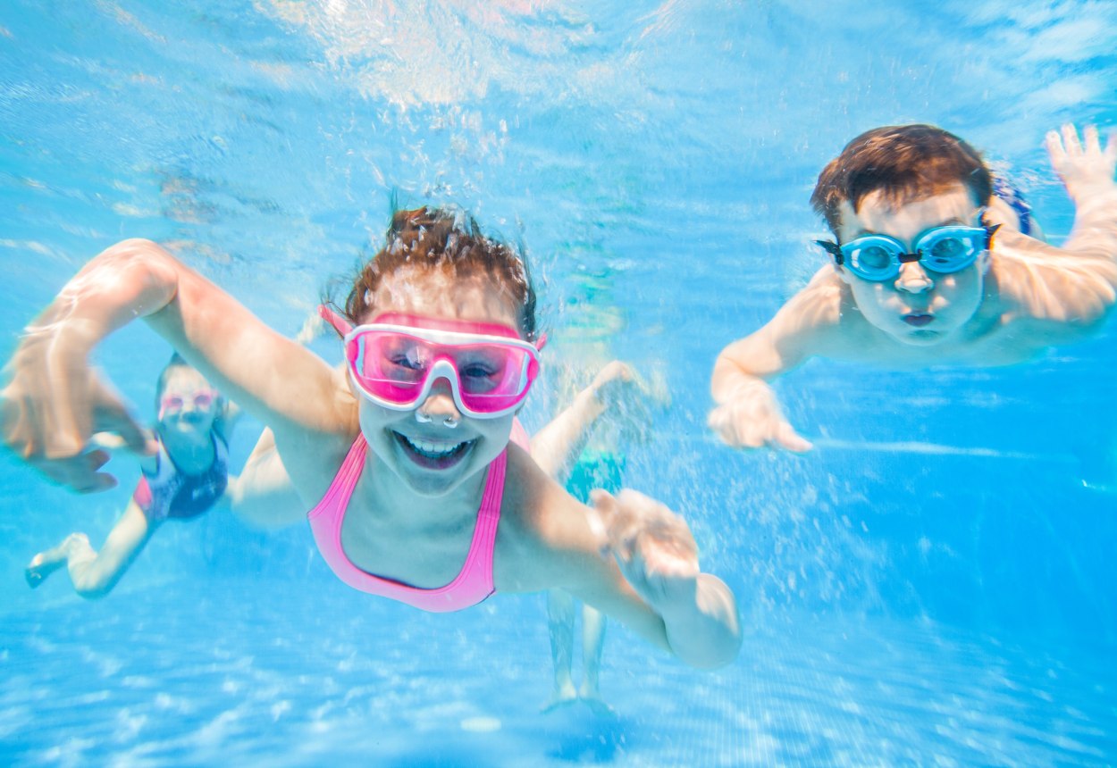 Zu sehen sind zwei Kinder mit Taucherbrillen unter Wasser in einem Schwimmbecken die lachen., © yanlev - stock.adobe.com