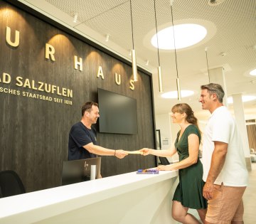 Drei Personen stehen im Eingangsbereich des Kurhaus Bad Salzuflen. Ein Mann steht hinter dem Tresen und reicht dem P&auml;rchen &uuml;ber diesen hinweg eine Eintrittskarte , &copy; Teutoburger Wald Tourismus / Stadt Bad Salzuflen / D.Ketz