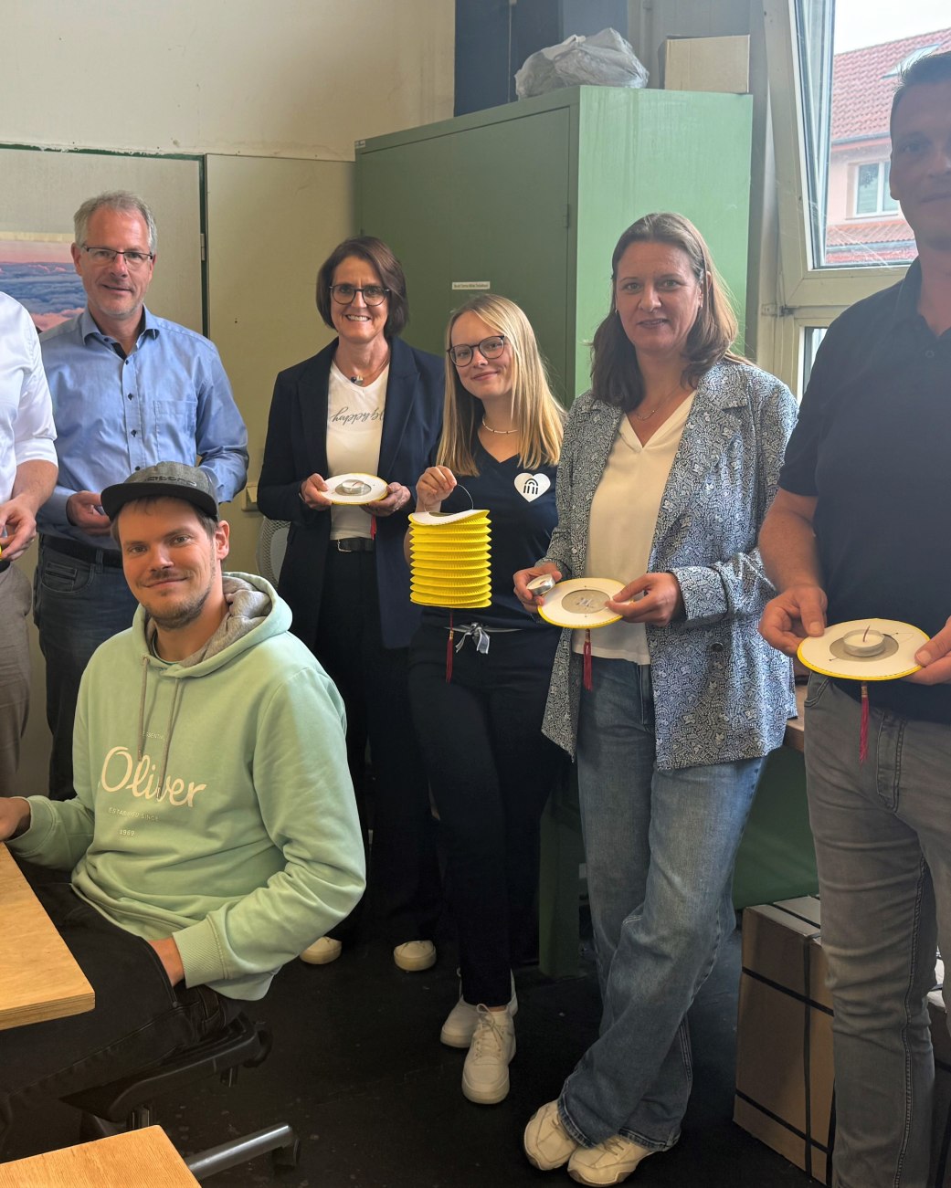 Neues Sozialprojekt der Stadt Bad Salzuflen mit der „Lebenshilfe Detmold e.V. Werre Werkstatt“ für die „Nacht
der 10.000 Kerzen“ am 29. August 2025: Werre Werkstatt-Mitarbeiter Eduard Peters (sitzend) verklebt an seinem Arbeitsplatz
Teelichter mit Zuglaternen. Die fertigen Laternen präsentieren voller Freude (stehend von links) Maximilian Seidel
(Kaufmännischer Vorstand Detmolder Lebenshilfe e.V. Werre Werkstatt), Udo Schwens (Werkstattleiter Detmolder Lebenshilfe e.V.), Myriam Heidemann (Fachdienstleitung Kulturelle Bildung, Event und Stadtmarketing), Francesca Rackow
(Projektmanagerin Eventabteilung Stadt Bad Salzuflen), Stephanie Kleine (Pädagogische Vorständin Detmolder Lebenshilfe e.V. Werre Werkstatt) und Stefan Gehrmann (Arbeitsvorbereitung & Auftragsverwaltung Detmolder Lebenshilfe e.V.
Werre Werkstatt)., © Stadt Bad Salzuflen Neues Sozialprojekt der Stadt Bad Salzuflen mit der „Lebenshilfe Detmold e.V. Werre Werkstatt“ für die „Nacht
der 10.000 Kerzen“ am 29. August 2025: Werre Werkstatt-Mitarbeiter Eduard Peters (sitzend) verklebt an seinem Arbeitsplatz
Teelichter mit Zuglaternen. Die fertigen Laternen präsentieren voller Freude (stehend von links) Maximilian Seidel
(Kaufmännischer Vorstand Detmolder Lebenshilfe e.V. Werre Werkstatt), Udo Schwens (Werkstattleiter Detmolder Lebenshilfe e.V.), Myriam Heidemann (Fachdienstleitung Kulturelle Bildung, Event und Stadtmarketing), Francesca Rackow
(Projektmanagerin Eventabteilung Stadt Bad Salzuflen), Stephanie Kleine (Pädagogische Vorständin Detmolder Lebenshilfe e.V. Werre Werkstatt) und Stefan Gehrmann (Arbeitsvorbereitung & Auftragsverwaltung Detmolder Lebenshilfe e.V.
Werre Werkstatt)., © Stadt Bad Salzuflen