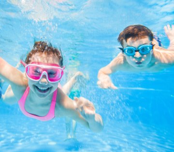 Zu sehen sind zwei Kinder mit Taucherbrillen unter Wasser in einem Schwimmbecken die lachen., © yanlev - stock.adobe.com