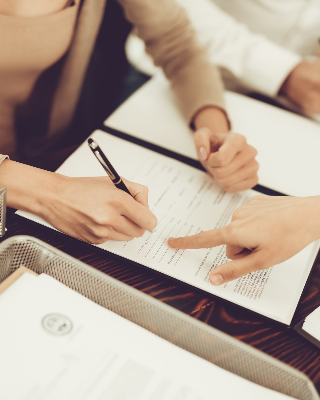 Auf dem Bild sind drei Personen zu sehen. Sie sitzen um einen Schreibtisch und haben Unterlagen auf dem Tisch ausgebreitet. Eine Person ist dabei ihre Unterschrift zu setzen. Es wird ein Vertrag &uuml;ber eine au&szlig;ergerichtliche Beilegung einer Streitigkeit aufgesetzt., &copy; VadimGuzhva - stock.adobe.com