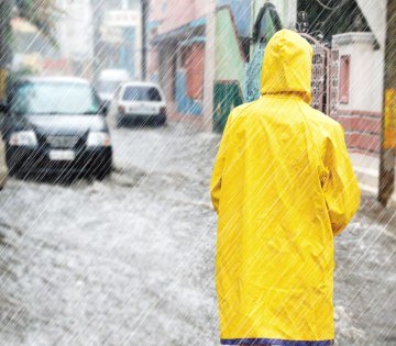 Starker Regen hat eine Straße überflutet, im Vordergrund ist eine Person mit gelben Regenmantel zu sehen., © Jürgen Fälchle - stock.adobe.com