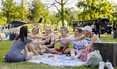 Eine Gruppe von Menschen sitzt auf einer Picknick-Decke im Kurpark und trinkt Wein bei einer Veranstaltung., © Stadt Bad Salzuflen | M. Gnoth