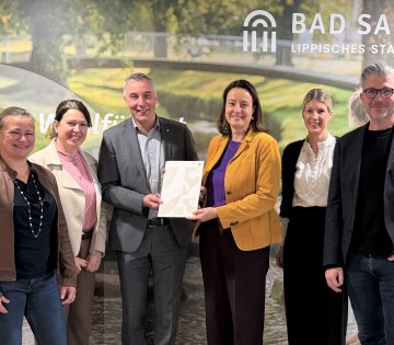 Neuer Meilenstein f&uuml;r die touristische Weiterentwicklung in Bad Salzuflen: Regierungspr&auml;sidentin Anna Katharina B&ouml;lling (3.v.r.) &uuml;bergab den F&ouml;rderbescheid f&uuml;r das Zukunftsprojekt &bdquo;Erlebniswelt Kneipp&ldquo; im Landschaftsgarten an B&uuml;rgermeister Dirk Tolkemitt (3.v.l.), Melanie Koring (2.v.r., Erste Beigeordnete & Stadtk&auml;mmerin), Ulrike Niebuhr (links, Technische Beigeordnete), Ralf Hammacher (rechts, Fachbereichsleitung Tourismus, Gesundheit, Kultur) und Katja M&ouml;nnigmann-Steinbeck (2.v.l., Fachbereichsleitung Jugend, Soziale Dienste, Schule). , &copy; Stadt Bad Salzuflen