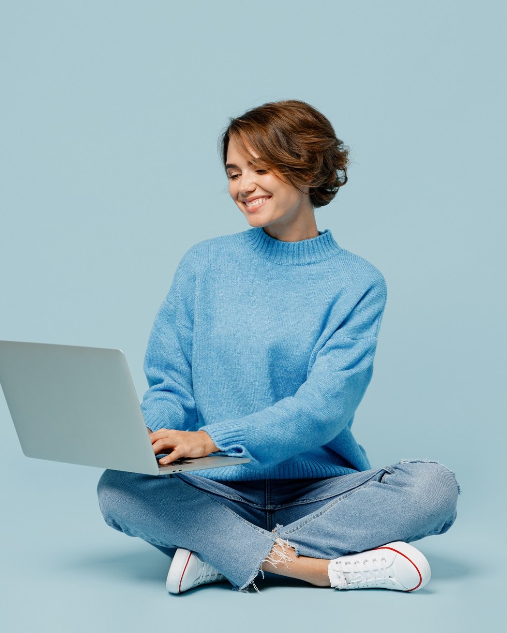 Frau sitzt im Schneidersitz auf dem Boden und schaut auf das aufgeklappte Notebook, das auf ihrem Scho&szlig; liegt, &copy; Adobe Stock