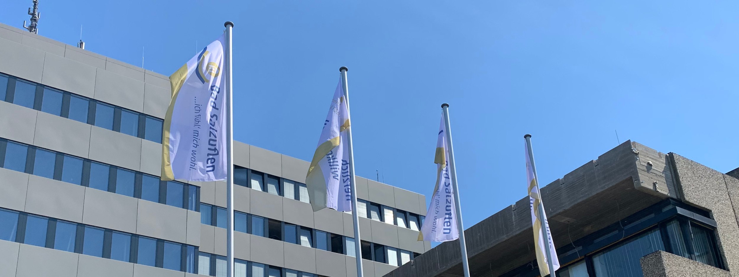 Vier Fahnen hängen an Fahnenmasten im Wind vor dem Rathaus der Stadt. Die Fahnen haben die Aufschriften - Bad Salzuflen...ich fühl mich wohl - und - Herzlich Willkommen - , © Stadt Bad Salzuflen