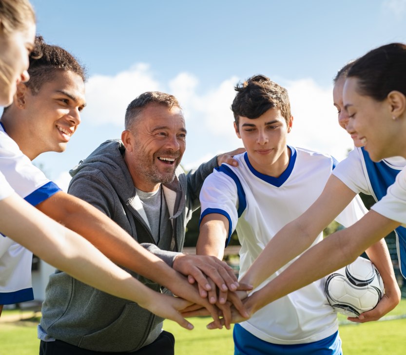 Sportler und Sportlerinnen stehen im Kreis zusammen und legen die Hände aufeinander., © stock.adobe.com - Rido