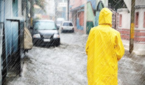 Starker Regen hat eine Straße überflutet, im Vordergrund ist eine Person mit gelben Regenmantel zu sehen., © Jürgen Fälchle - stock.adobe.com