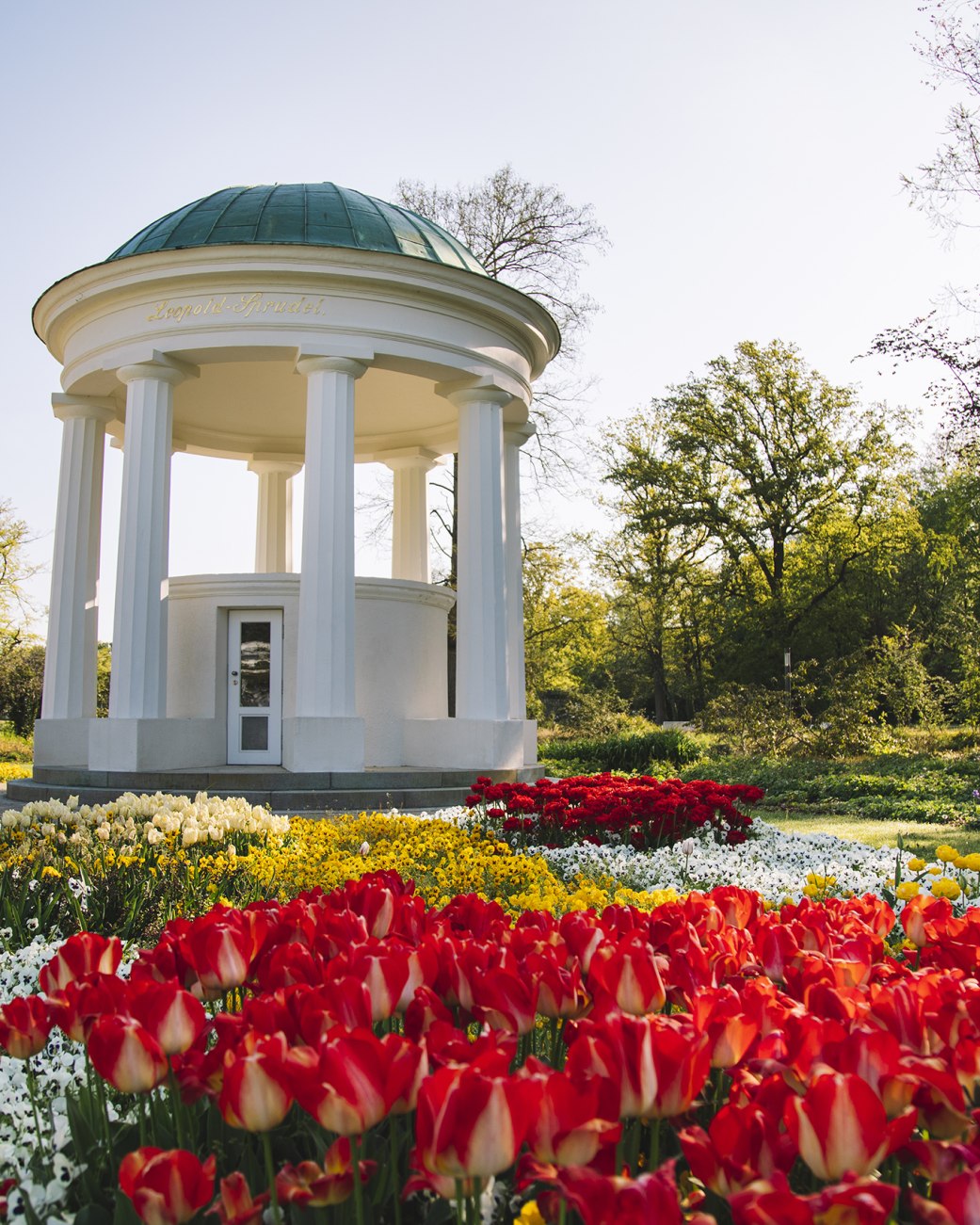 Zu sehen ist der Tempel des Leopoldsprudels im Kurpark, im Vordergrund sind blühende Blumen zu sehen, die Sonne scheint, © Stadt Bad Salzuflen - Nadja Jacke